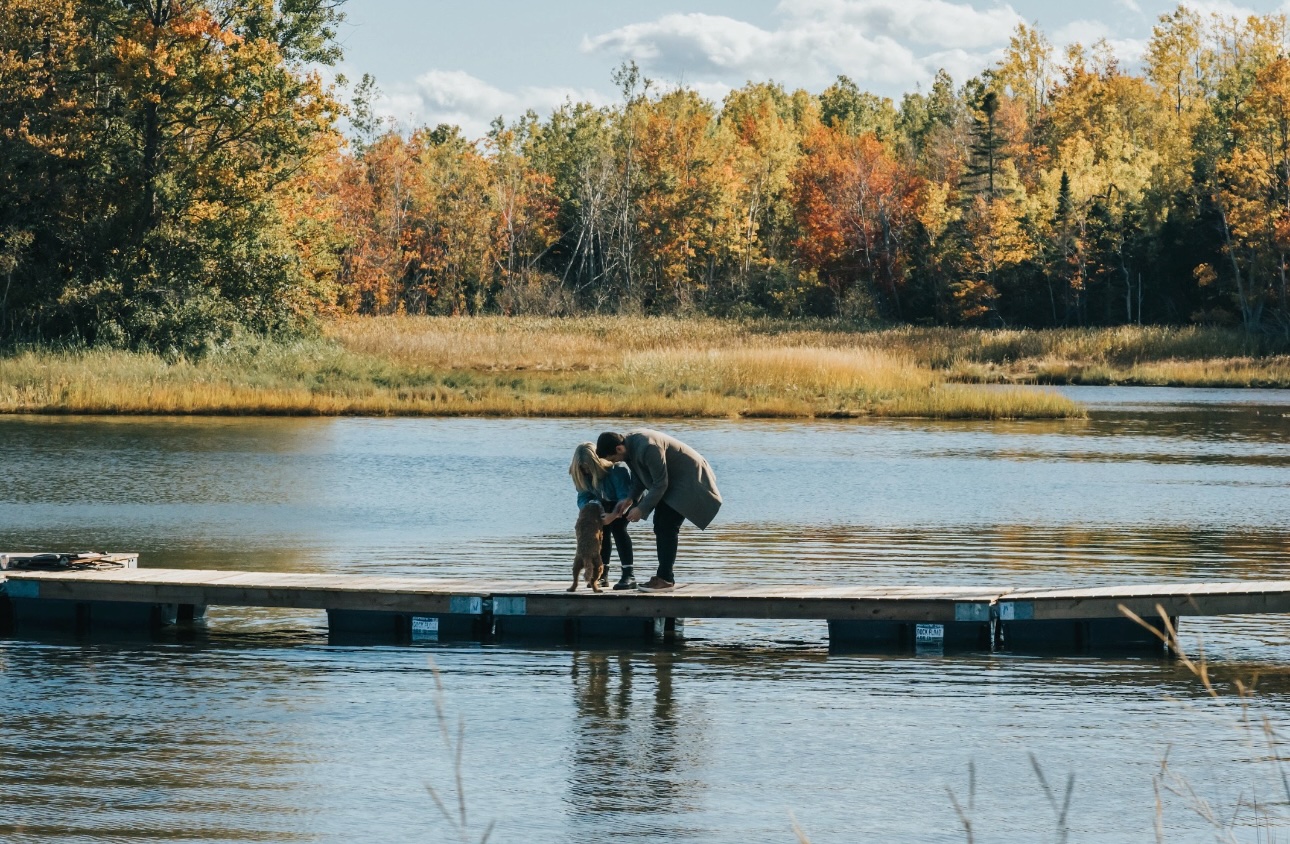 Amanda, Alex, and their dog on a dock by the water on a golden autumn day